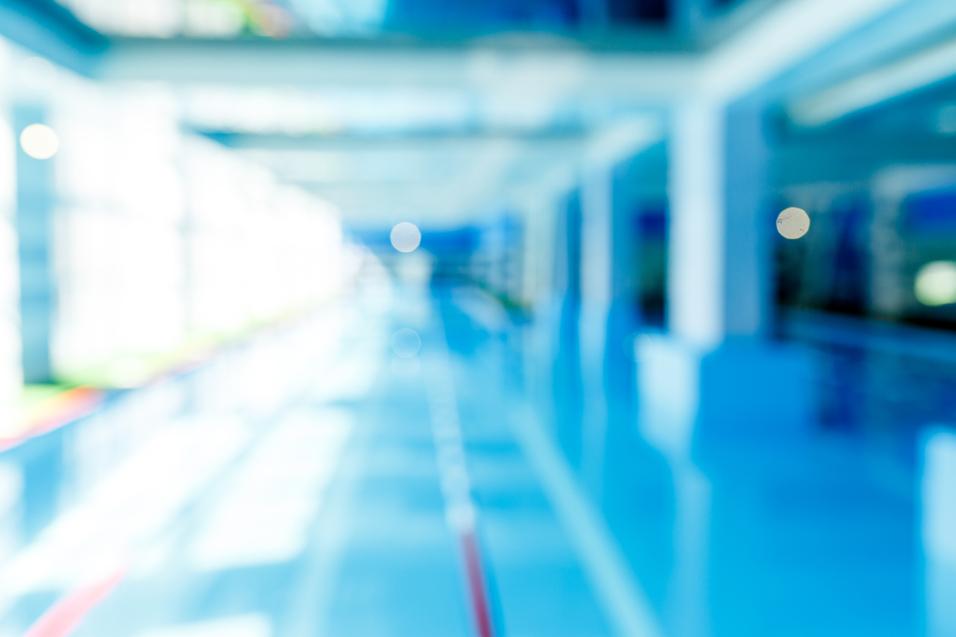 Unscharfes Bild eines modernen Schwimmbeckens mit blauer Wasseroberfläche und hellem, lichtdurchflutetem Raum.